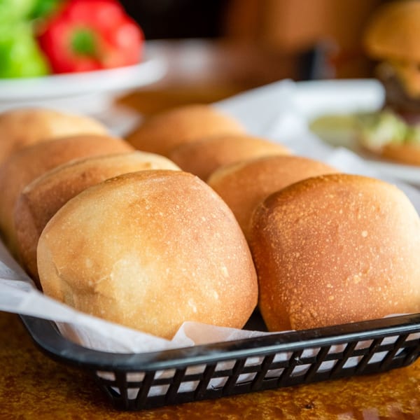 Freshly baked dinner rolls in a black basket lined with white paper, ready to be served.