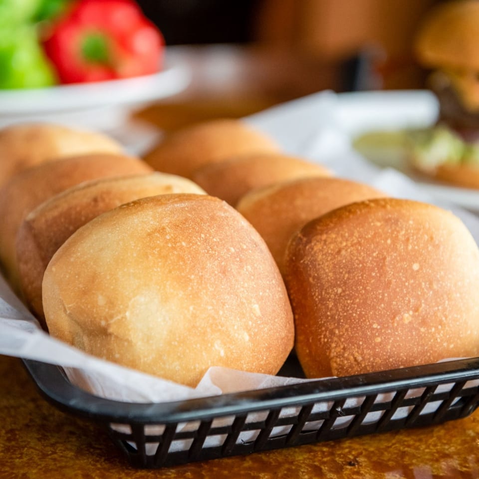 Freshly baked dinner rolls in a black basket lined with white paper, ready to be served.