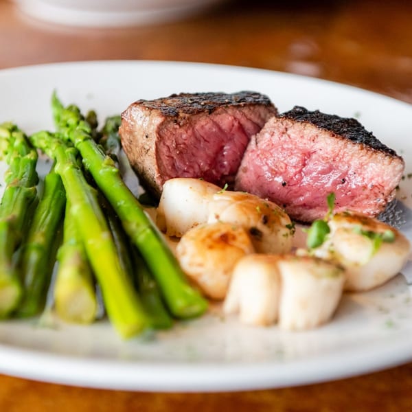 Christopher's Steakhouse and Seafood's medium-rare steak, seared scallops, and green asparagus on a white plate.