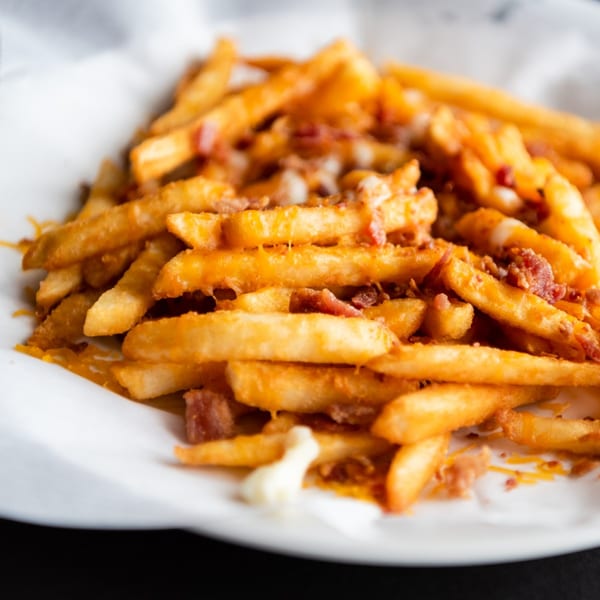 Golden french fries topped with melted cheese and crispy bacon bits in a white paper-lined basket.