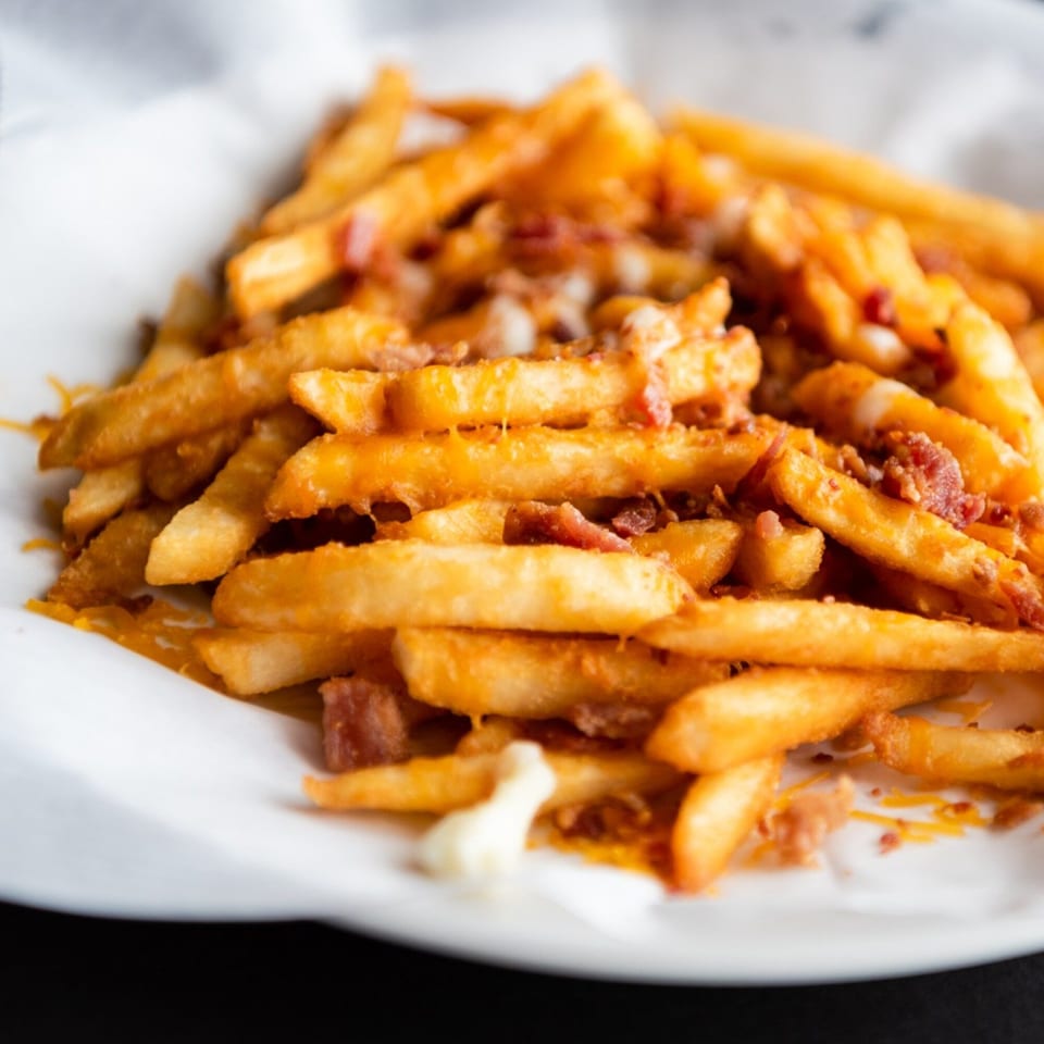 Golden french fries topped with melted cheese and crispy bacon bits in a white paper-lined basket.