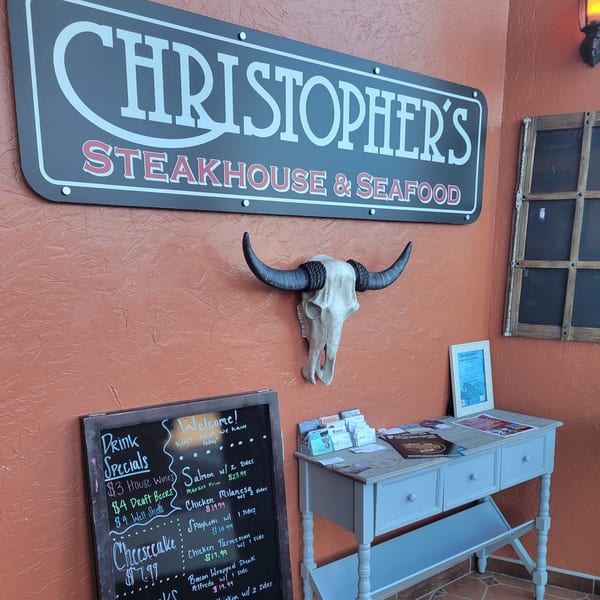 Christopher's Steakhouse and Seafood sign above a bull skull, chalkboard menu, and small table.