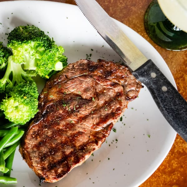 Grilled steak with broccoli and green beans on a white plate with a steak knife.
