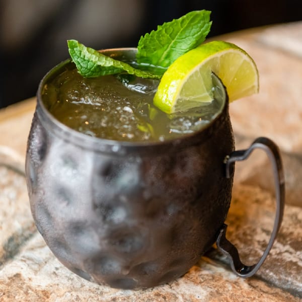 A dark metal mug filled with a green cocktail, garnished with fresh mint and a lime wedge.