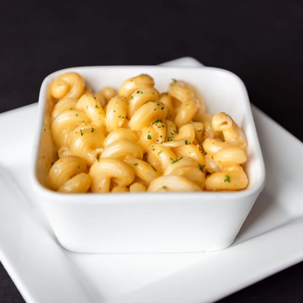 Creamy macaroni and cheese with parsley flakes in a white square bowl on a white plate.