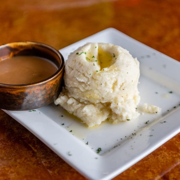 Creamy mashed potatoes with melted butter and gravy in a copper bowl on a white plate.