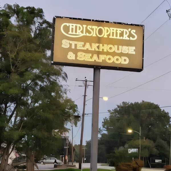 Illuminated sign for Christopher's Steakhouse & Seafood, surrounded by trees and power lines at dusk.