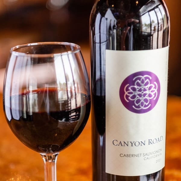 A glass of red wine next to a bottle of Canyon Road Cabernet Sauvignon.
