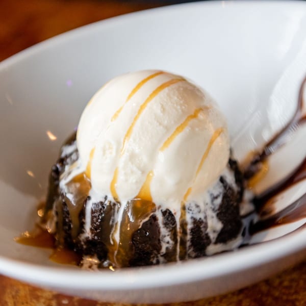 Warm chocolate lava cake topped with vanilla ice cream and caramel drizzle in a white bowl.